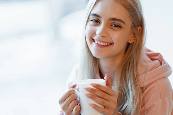 Giovane ragazza bionda sorride mentre ha in mano una tazza di tè fumante 