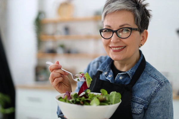 Donna con capelli corti e occhiali mangia da una bowl di insalata