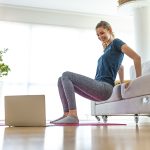Donna che si allena a casa e osserva al computer un video tutorial sull’hip thrust