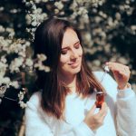 Donna in mezzo a fiori profumati che annusa una boccetta di oli essenziali