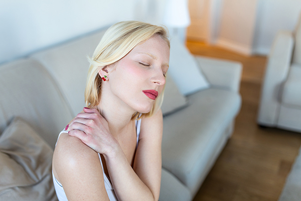 Donna con sintomi del linfoma di Hodgkin che massaggia il suo collo seduta sul divano di casa