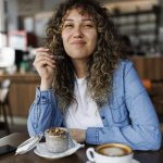 Giovane donna sorridente che mangia un budino con semi di chia per colazione seduta al tavolino di un bar