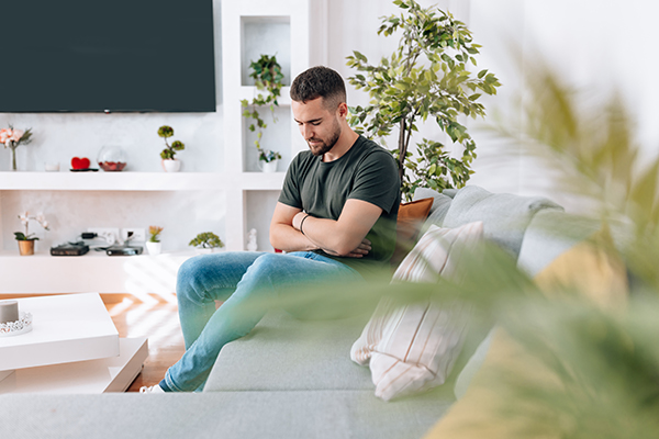 Uomo con l’IPMN del pancreas che si tocca la pancia mentre ricerca sollievo sul divano del suo appartamento