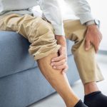 Uomo maturo seduto sul divano si massaggia le caviglie gonfie