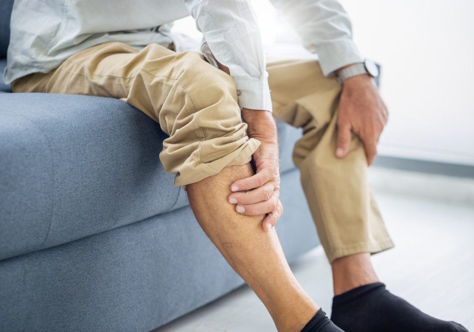 Uomo maturo seduto sul divano si massaggia le caviglie gonfie