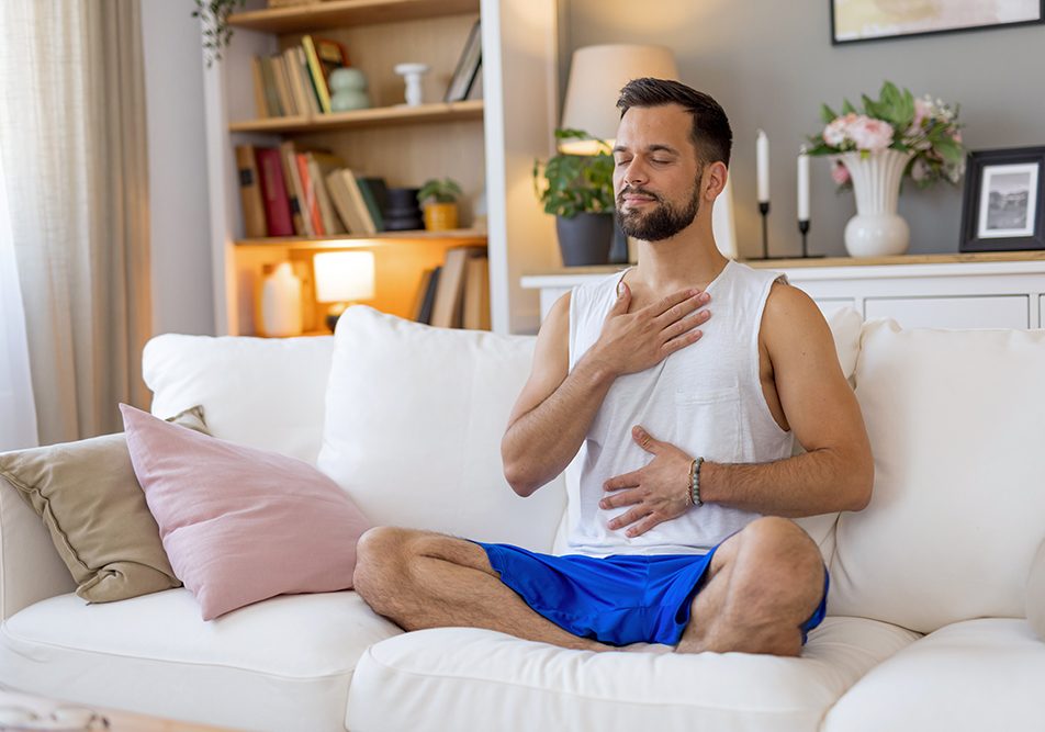 uomo-meditando-con-mani-su-petto-e-addome-cura-tumore-al-pancreas Uomo che medita sul divano con le mani sul petto e sull’addome, prendendosi cura del tumore al pancreas