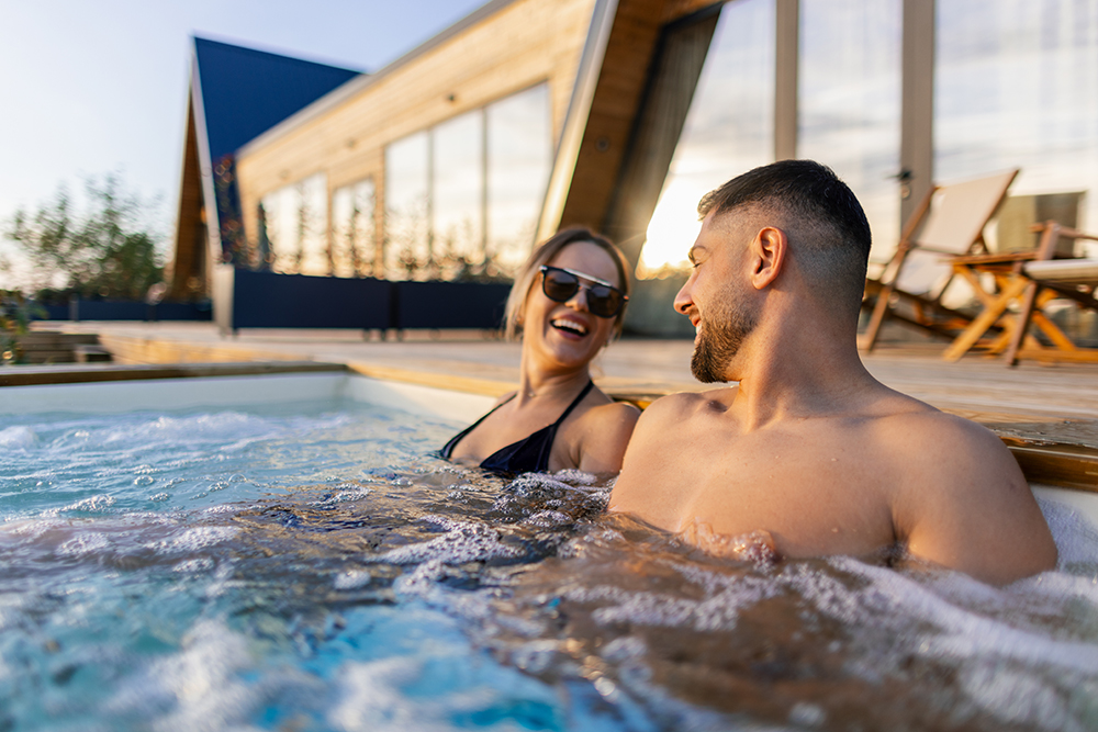 Coppia in una vasca idromassaggio della spa che si gode gli effetti di una balneoterapia osservando il tramonto