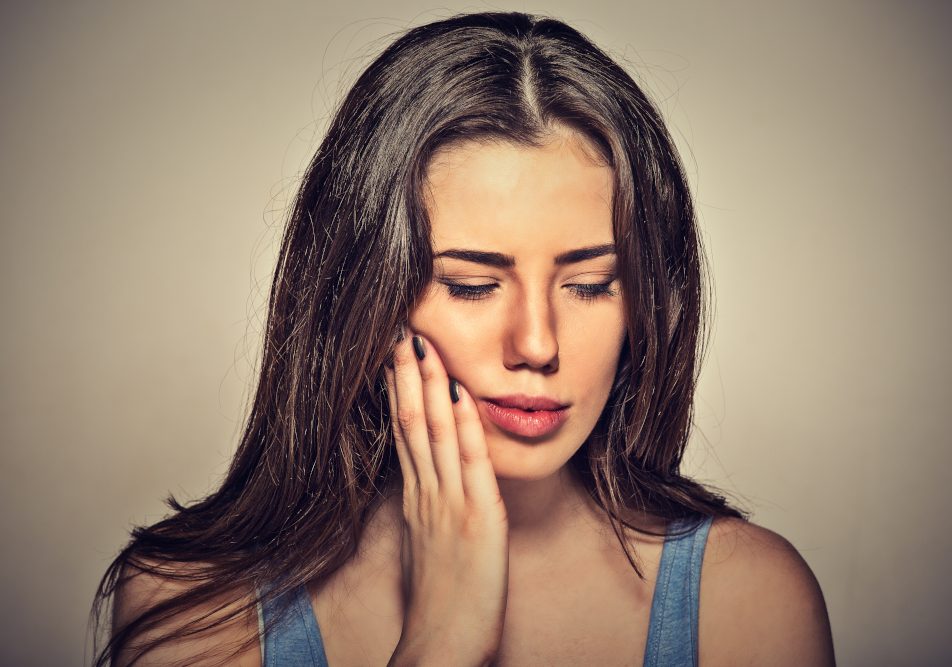 donna-con-ascesso-dentale Donna si tocca la guancia con la mano a causa di un ascesso dentale