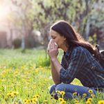 Donna che soffre di rinite allergica in un campo fiorito durante una passeggiata primaverile