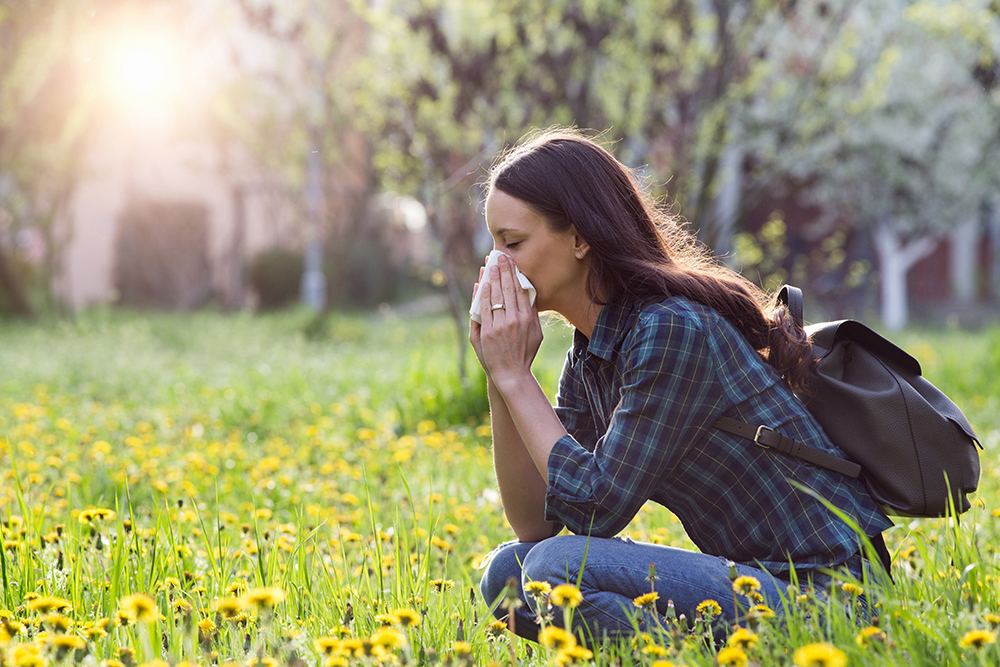 Donna che soffre di rinite allergica in un campo fiorito durante una passeggiata primaverile