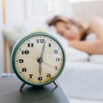Sveglia in primo piano e donna con ritmo circadiano regolare che dorme nel suo letto