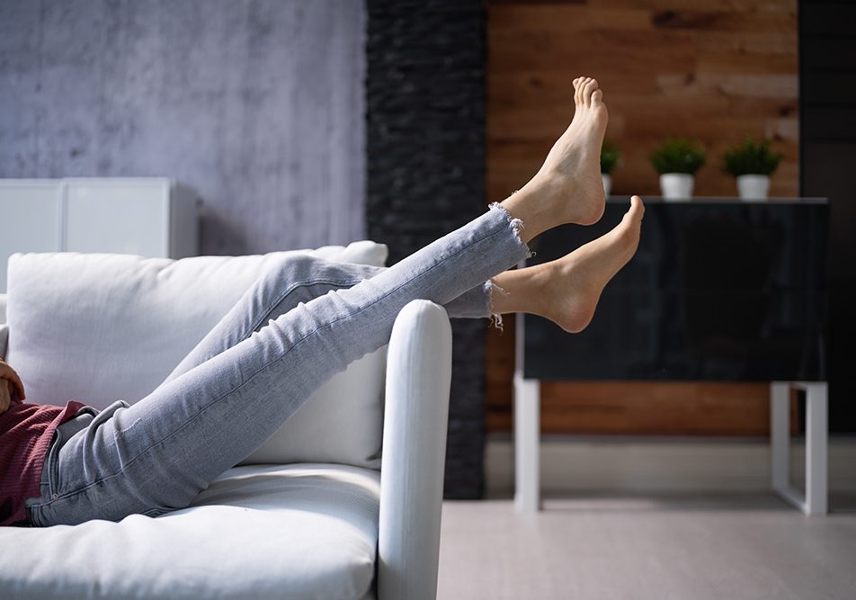 Donna sdraiata supina sul divano con le gambe alzate per fornire sollievo ai piedi gonfi