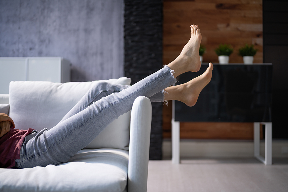 Donna sdraiata supina sul divano con le gambe alzate per fornire sollievo ai piedi gonfi