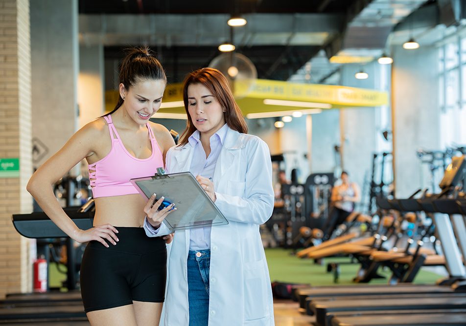 Atleta donna in palestra che conversa con la dottoressa durante la visita di medicina dello sport