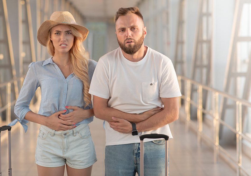 coppia-in-aeroporto-cercando-rimedi-mal-di-pancia Coppia che arriva in aeroporto munita di trolley e cerca rimedi per curare il mal di pancia