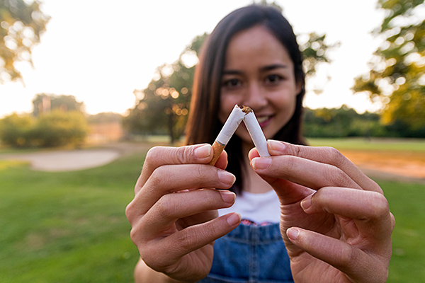 Giovane donna in un parco all’aperto che previene la rinite allergica smettendo di fumare e spezza una sigaretta