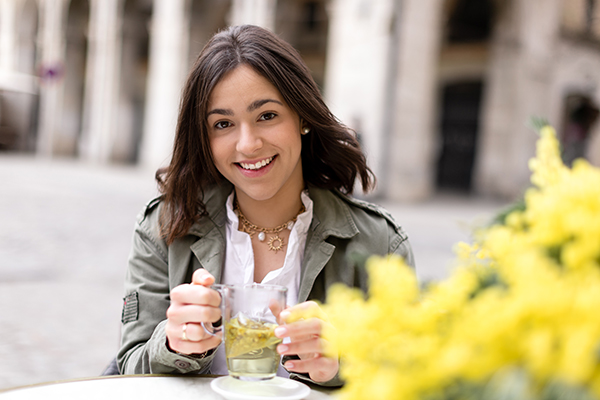 Giovane donna che beve da una tazza un infuso di camomilla, un rimedio naturale contro il mal di stomaco, nel dehors esterno di un bar