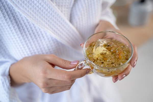 Donna in accappatoio che beve una tazza di tè alla camomilla, uno degli ansiolitici naturali più diffusi