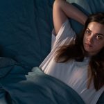 Giovane donna a letto che ha difficoltà a rilassarsi, tra i sintomi fisici dell'ansia notturna