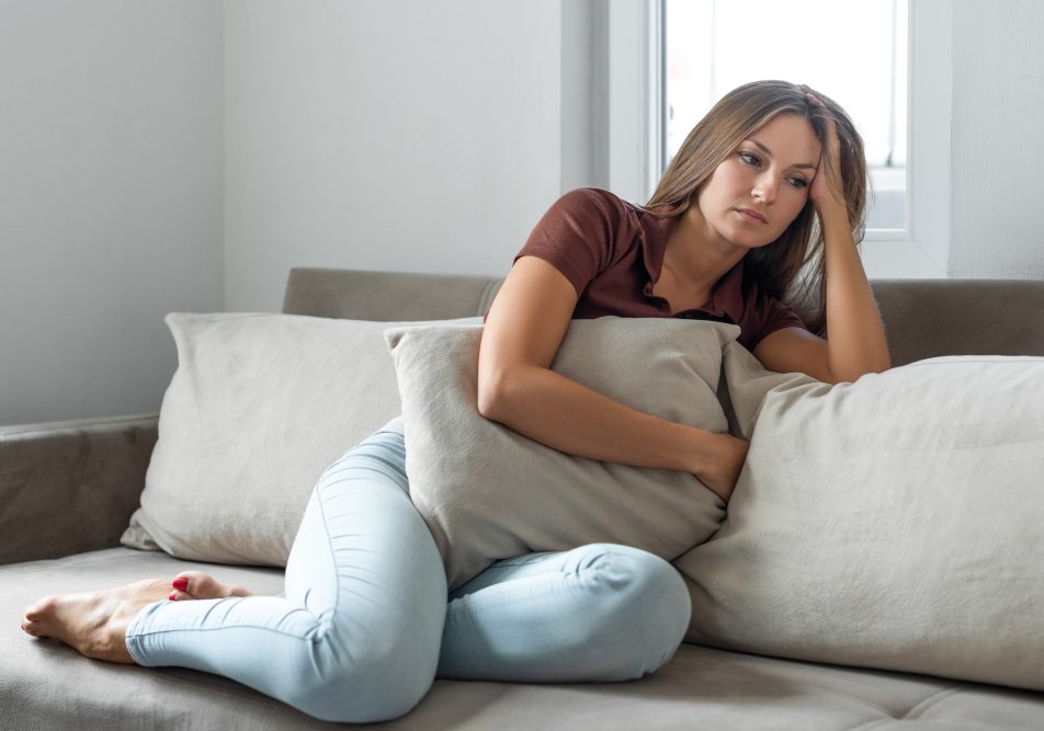 Donna seduta sul divano mostra sofferenza pe la nausea da ansia