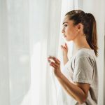 Donna apprensiva, con sintomi di ansia e depressione, che guarda fuori dalla finestra del salotto di casa