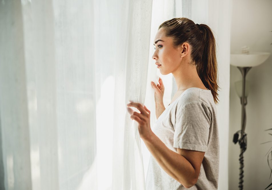 Donna apprensiva, con sintomi di ansia e depressione, che guarda fuori dalla finestra del salotto di casa