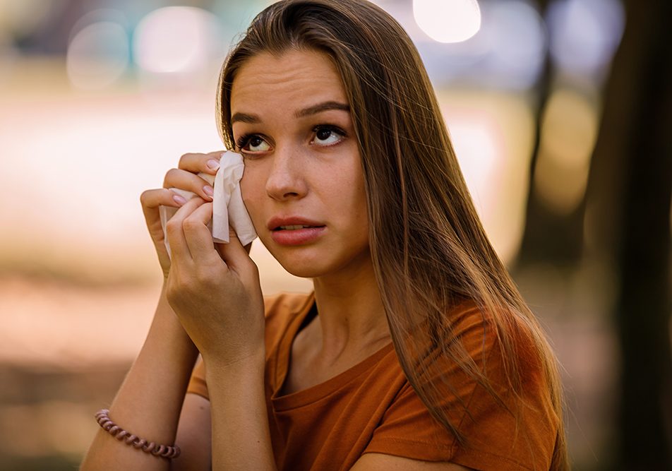 Donna al parco con una congiuntivite allergica che strofina gli occhi lacrimanti usando un fazzoletto
