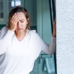 Donna in cucina che sperimenta sintomi di una crisi epilettica mentre si tocca la fronte e appoggia il palmo della mano al muro