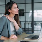 Donna nel suo ufficio che soffre di tensione muscolare, tra i sintomi fisici dell’ipertensione emotiva