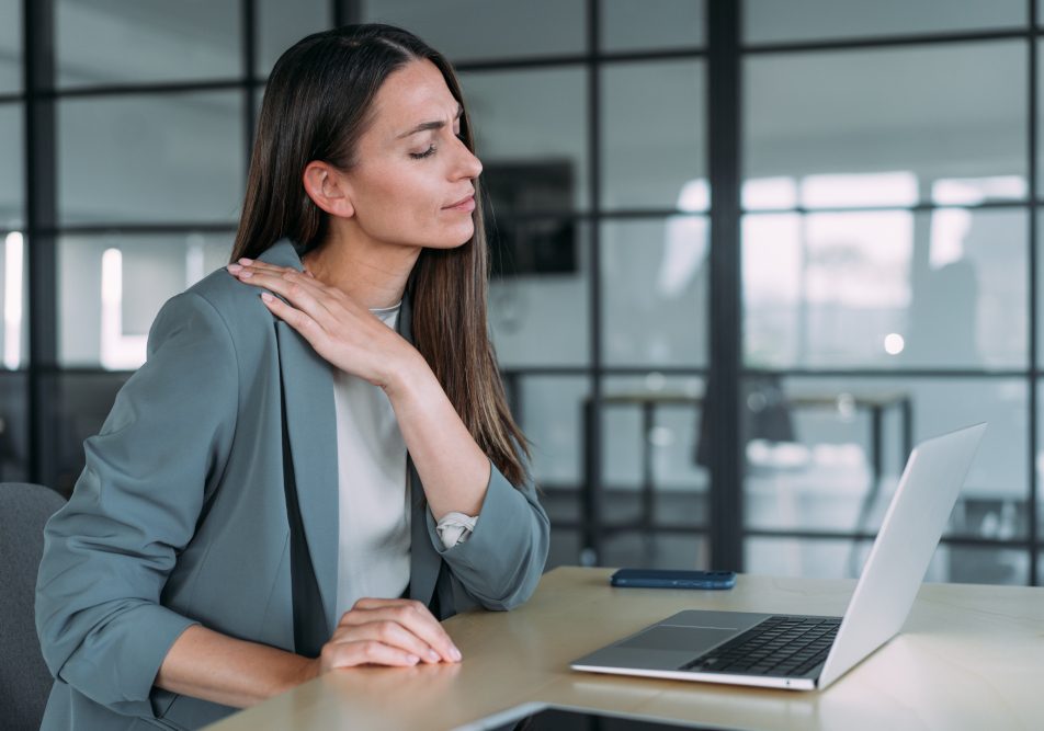 Donna nel suo ufficio che soffre di tensione muscolare, tra i sintomi fisici dell’ipertensione emotiva