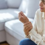 Donna sul suo divano si tiene la mano che trema, tra i sintomi del tremore da stress trema,
