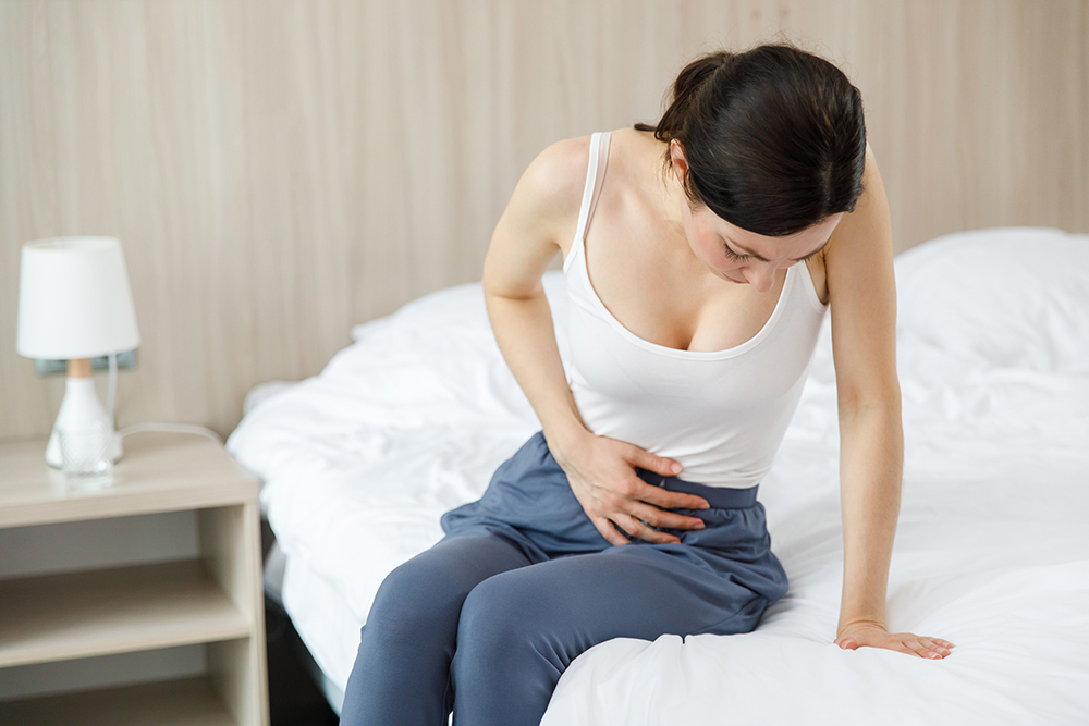 Tumore ovarico: a chi è consigliato il test genetico e come funziona 31 Giovane donna con sintomi del tumore alle ovaie seduta a letto che tocca il basso ventre dolorante con la mano
