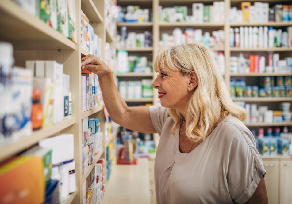 Donna matura tra gli scaffali di una farmacia per acquistare farmaci senza ricetta