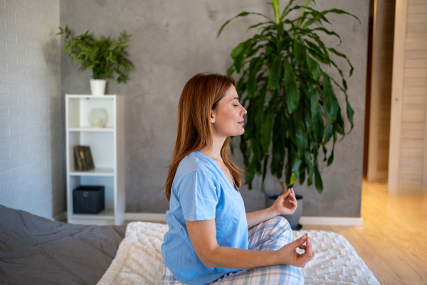 Donna seduta sul letto pratica tecniche di rilassamento per combattere l'ansia prima di dormire
