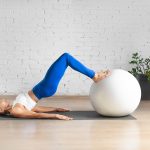 Giovane donna caucasica in una spaziosa sala per pilates che pratica ginnastica pelvica con l’ausilio di una fitball