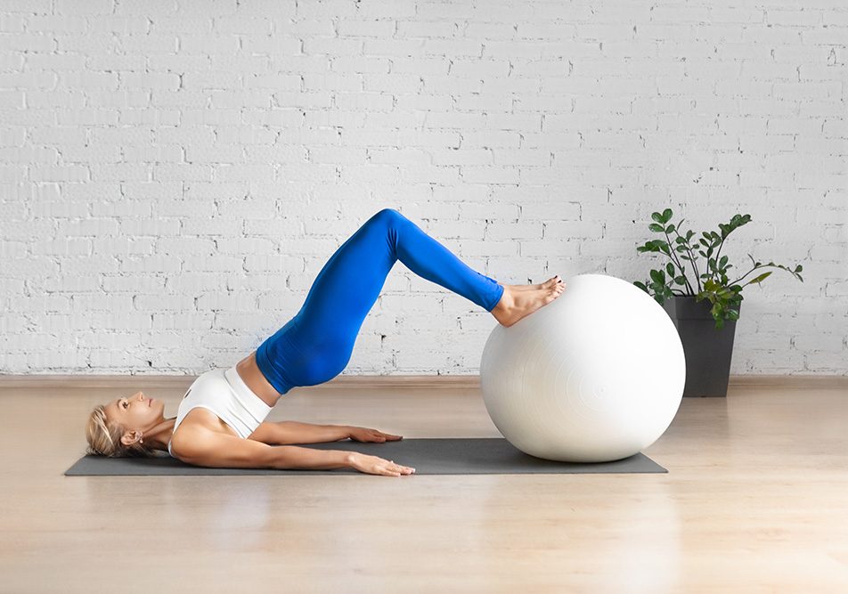 Giovane donna caucasica in una spaziosa sala per pilates che pratica ginnastica pelvica con l’ausilio di una fitball