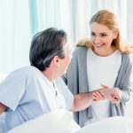 Donna in ospedale che fa visita al marito, aiutandolo a stare alzato nel letto in seguito al trapianto di midollo osseo