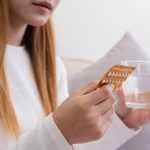 Giovane donna con bicchiere d'acqua in mano che sta assumendo pillola anticoncezionale