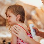 Mamma e figlia in estate sotto il sole proteggono con la crema e assorbono vitamine e minerali