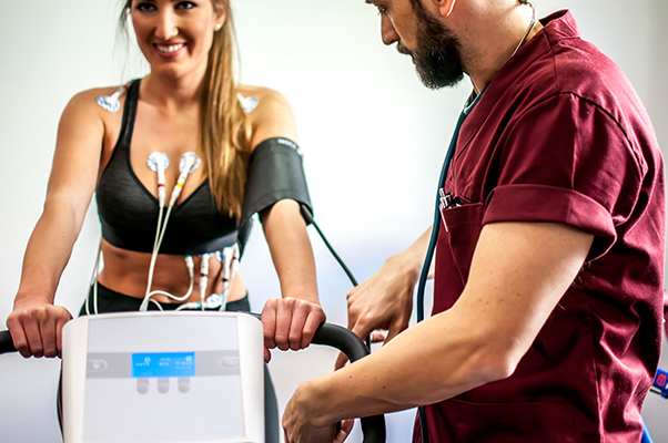 Medico che monitora l’elettrocardiogramma sotto sforzo su una paziente donna su una cyclette durante la visita medico sportiva