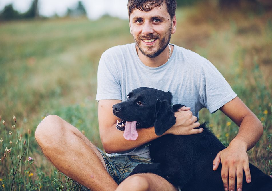 Padrone seduto in un prato in compagnia suo cane, un labrador retriever nero, prendendosi cura della sua leishmaniosi