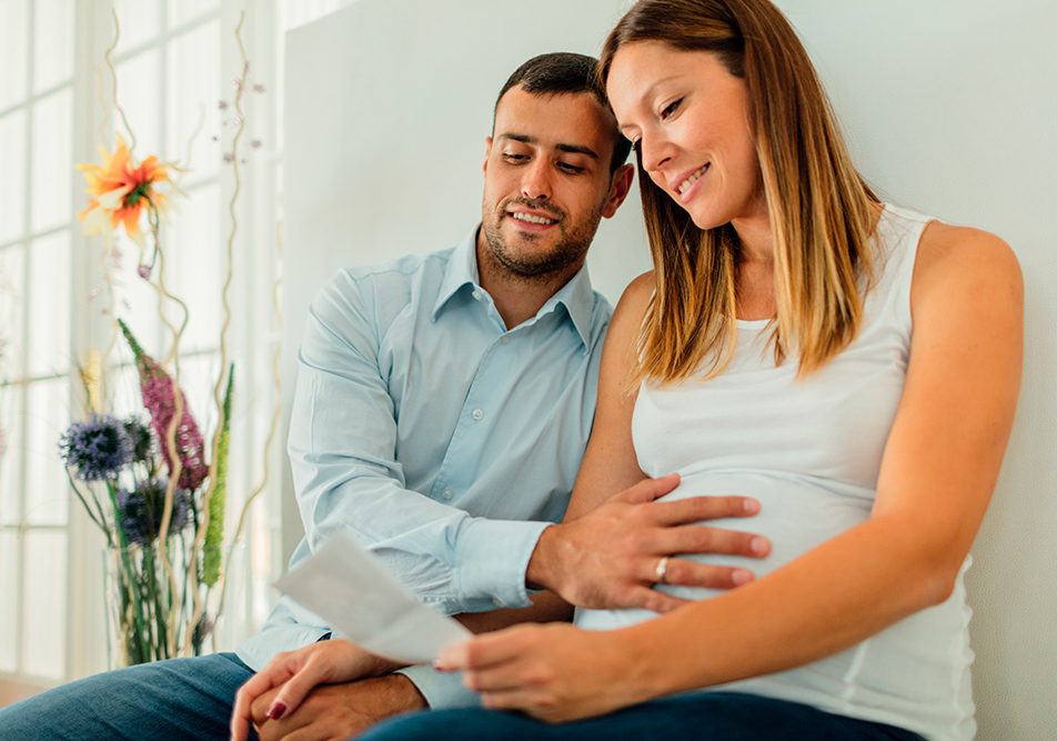 Paziente in gravidanza con la sclerosi multipla seduta nella sala di attesa di una clinica insieme al compagno, con cui legge gli esiti di un esame medico