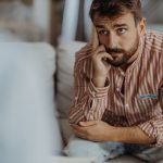 Paziente con sintomi d’ansia generalizzata, con uno sguardo leggermente preoccupato, seduto sul divano mentre si sottopone ad una seduta di psicoterapia