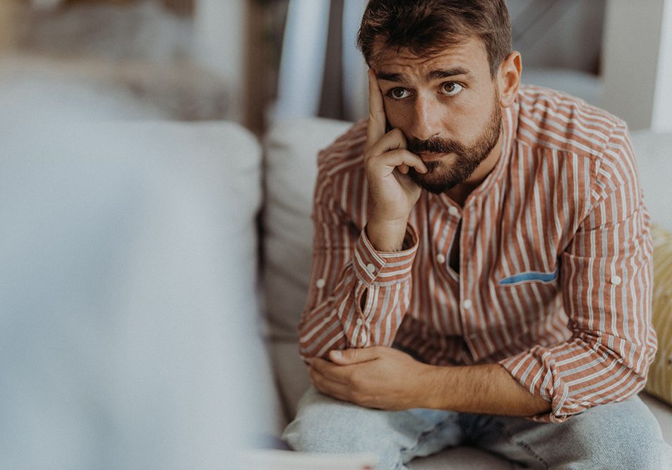 Paziente con sintomi d’ansia generalizzata, con uno sguardo leggermente preoccupato, seduto sul divano mentre si sottopone ad una seduta di psicoterapia