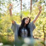 Ragazza nella foresta serena e rilassata mentre respira aria fresca, migliorando il suo contatto con la natura e il benessere