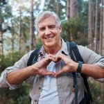 Uomo maturo che forma un cuore con le mani e previene i sintomi dell’infarto attraverso l’attività fisica ed escursioni nella natura