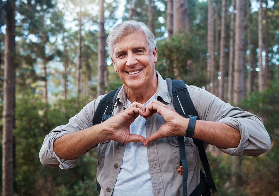 Uomo maturo che forma un cuore con le mani e previene i sintomi dell’infarto attraverso l’attività fisica ed escursioni nella natura