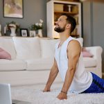Uomo sul tappeto, con davanti il suo laptop, sollevato dall’allungamento della colonna vertebrale attraverso esercizi mirati per il mal di schiena