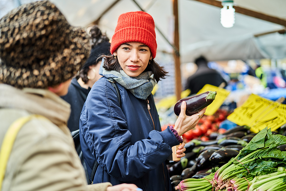 Amiche al mercato rionale che acquistano verdura autunnale, tra cui melanzane