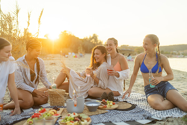 Gruppo di amiche divertite in spiaggia che consuma dei piatti freddi estivi
